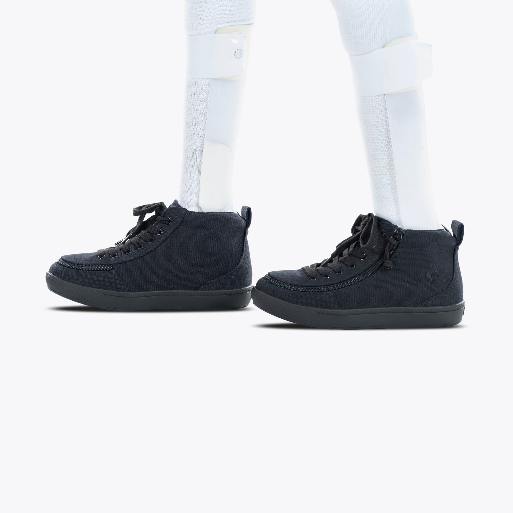 A person wears white leg braces and socks with BILLY Footwear's Black to the Floor BILLY Classic D|R II High sneakers. These black high-tops have black soles and a wide toe box, making them AFO-friendly. Shown on a plain white background.