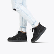A person wearing light blue ripped skinny jeans and Black to the Floor BILLY CS High shoes by BILLY Footwear stands against a plain white background, with only their lower legs and feet visible.