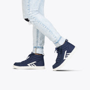 Wearing light-wash ripped skinny jeans and Navy/White BILLY CS High sneakers by BILLY Footwear with white soles and arrow designs, a person steps forward against a white background.