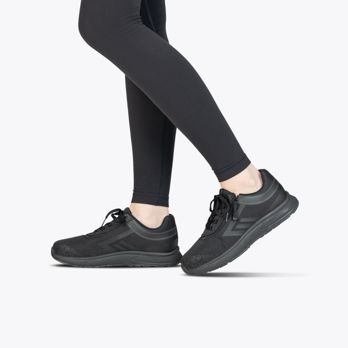 A person wearing Black to the Floor BILLY Sport Inclusion shoes from BILLY Footwear and black leggings stands on a light gray background, with only their legs and feet visible.