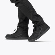 A person in black pants and the Men's Black to the Floor BILLY CS High sneakers by BILLY Footwear, featuring the Full Wrap Zipper design, is walking—shown from the knees down against a plain light background.